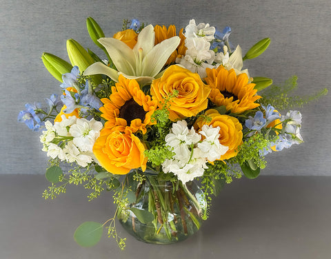 Golden Glow Summer Floral Centerpiece – Sunflowers, Yellow Roses & White Lilies in Glass Vase